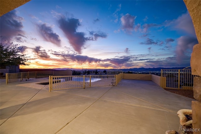 patio terrace at dusk with a fenced in pool, fence, and a mountain view