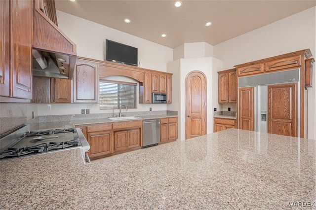 kitchen featuring light stone counters, recessed lighting, stainless steel appliances, a sink, and brown cabinetry