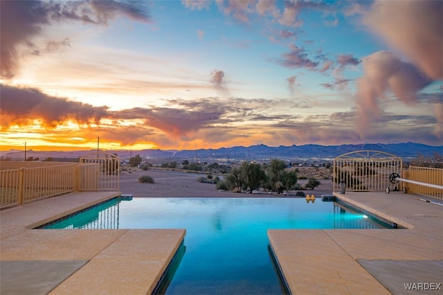 pool at dusk with a mountain view, a fenced in pool, and a patio