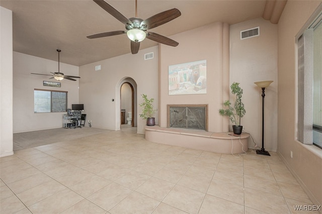 unfurnished living room featuring arched walkways, visible vents, a fireplace with raised hearth, and light tile patterned floors