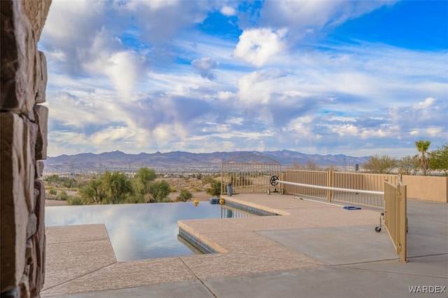 outdoor pool with a patio area, a mountain view, and fence