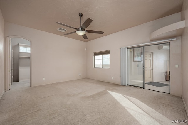 unfurnished bedroom with arched walkways, multiple windows, visible vents, and light colored carpet