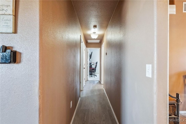 corridor featuring visible vents, baseboards, wood finished floors, and a textured wall