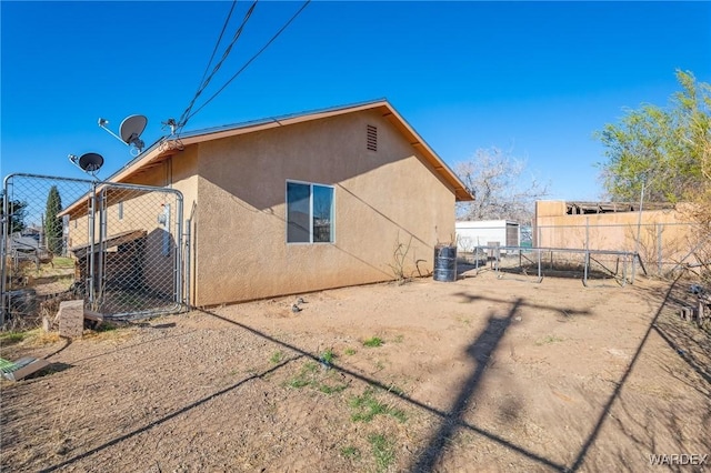 rear view of property featuring fence, a gate, and stucco siding