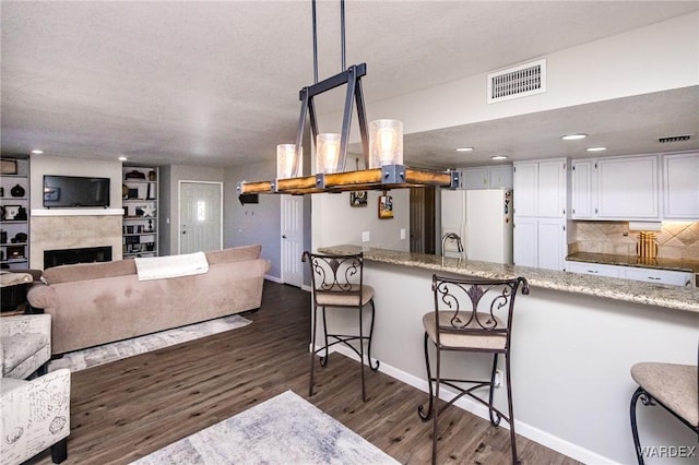 kitchen featuring decorative light fixtures, visible vents, open floor plan, white cabinetry, and white fridge with ice dispenser