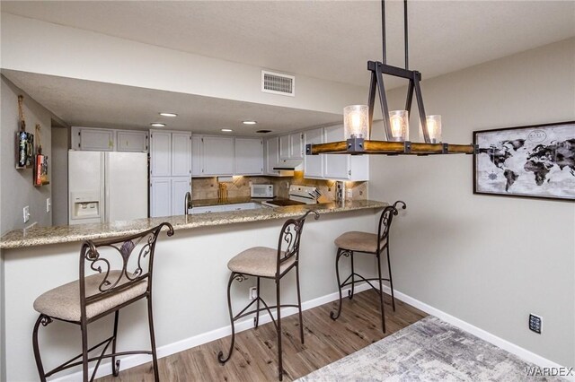 kitchen featuring a peninsula, visible vents, range, white fridge with ice dispenser, and decorative light fixtures