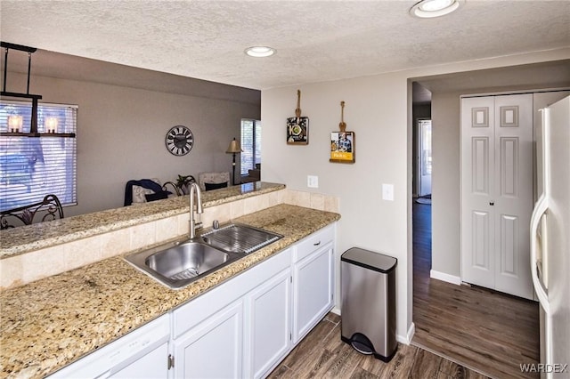 kitchen featuring white appliances, white cabinets, dark wood-style flooring, hanging light fixtures, and a sink