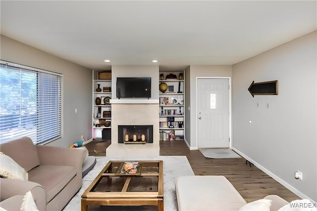 living room featuring recessed lighting, a fireplace with raised hearth, baseboards, and wood finished floors