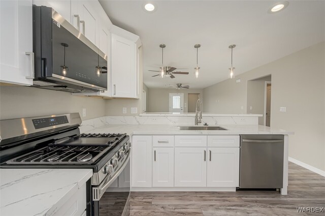 kitchen with a peninsula, a sink, white cabinets, appliances with stainless steel finishes, and decorative light fixtures