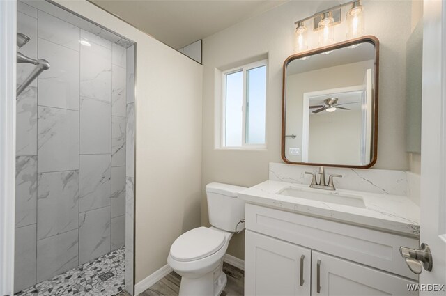 bathroom with toilet, tiled shower, vanity, and baseboards