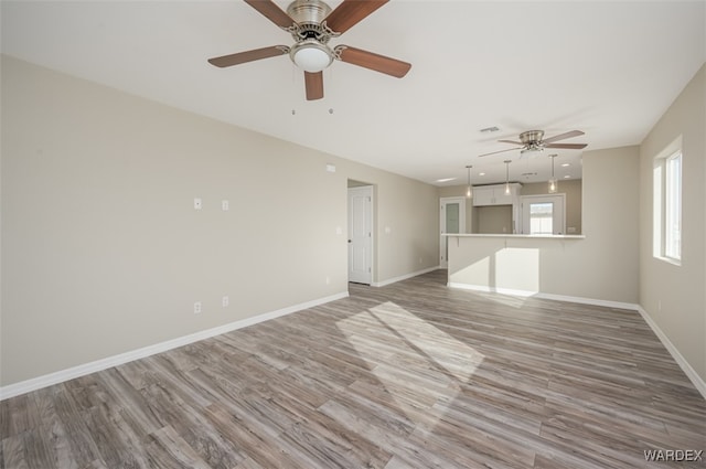 unfurnished living room with a ceiling fan, wood finished floors, visible vents, and baseboards