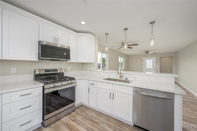 kitchen featuring white cabinets, appliances with stainless steel finishes, a peninsula, light wood-type flooring, and a sink