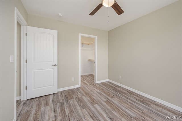 unfurnished bedroom featuring baseboards, ceiling fan, a walk in closet, light wood-type flooring, and a closet