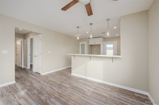 kitchen with white cabinetry, light countertops, light wood-type flooring, a kitchen bar, and decorative light fixtures