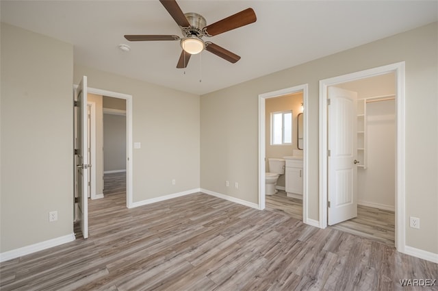 unfurnished bedroom featuring a spacious closet, light wood finished floors, connected bathroom, and baseboards