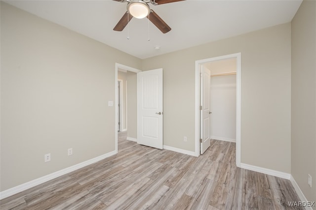 unfurnished bedroom with a closet, a spacious closet, a ceiling fan, light wood-type flooring, and baseboards