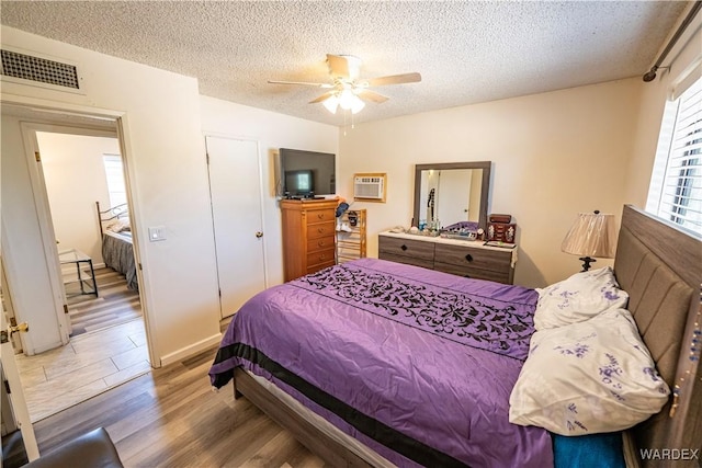 bedroom featuring a textured ceiling, a ceiling fan, wood finished floors, visible vents, and a wall mounted AC
