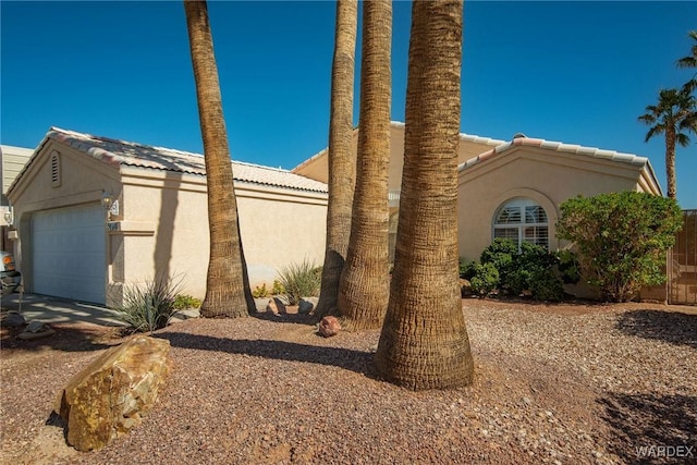 view of side of property featuring a garage, a tile roof, and stucco siding