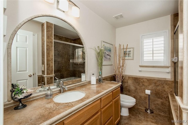 full bath with vanity, a wainscoted wall, a tile shower, tile walls, and toilet