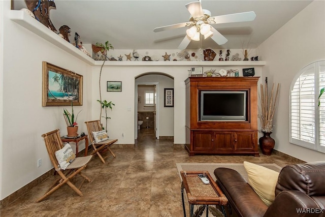 living room featuring baseboards, arched walkways, and a ceiling fan