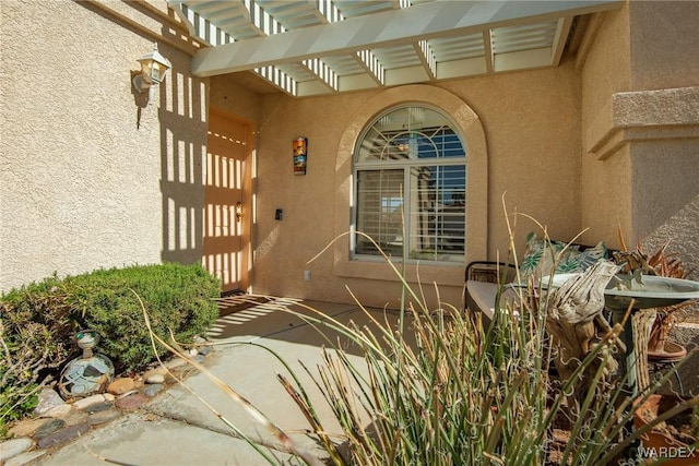 doorway to property featuring stucco siding and a pergola