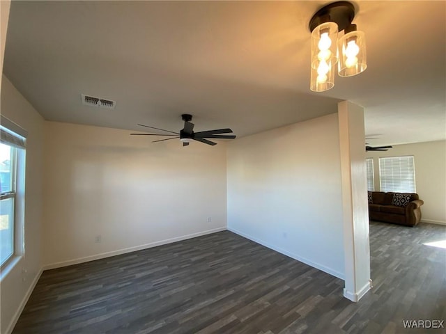 unfurnished room featuring baseboards, ceiling fan with notable chandelier, dark wood-style floors, and visible vents