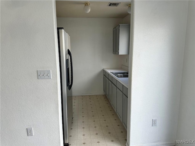 kitchen with light floors, gray cabinets, light countertops, visible vents, and freestanding refrigerator