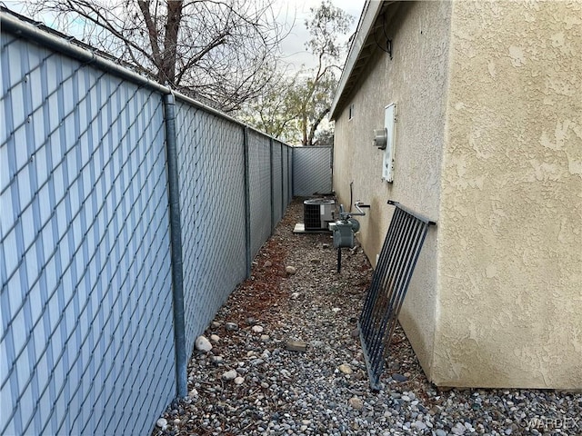 view of side of property featuring central AC unit, fence, and stucco siding