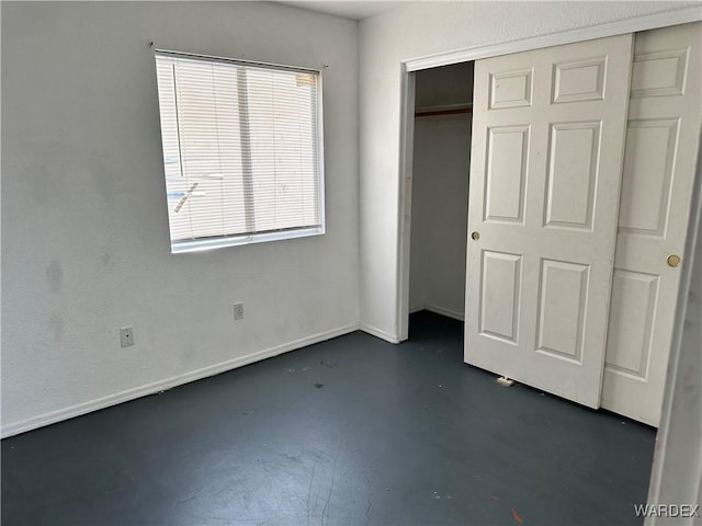 unfurnished bedroom with finished concrete flooring, a closet, and baseboards