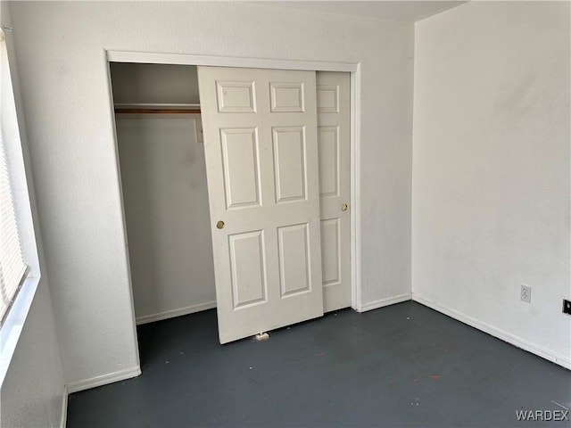 unfurnished bedroom with finished concrete flooring, a closet, and baseboards