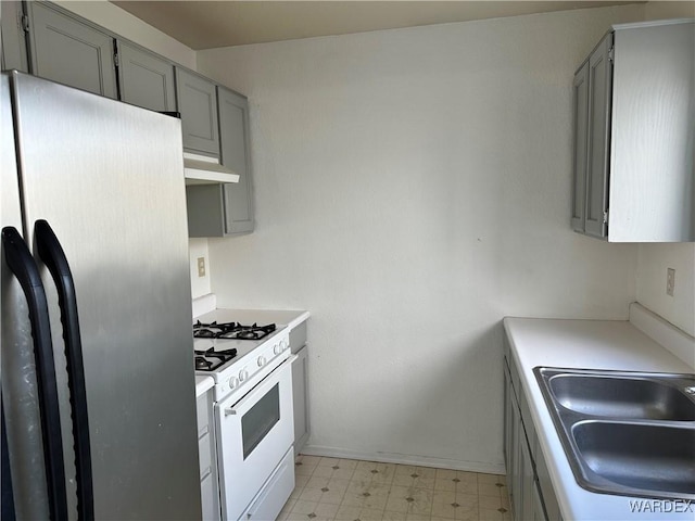 kitchen with white gas stove, a sink, light countertops, freestanding refrigerator, and light floors