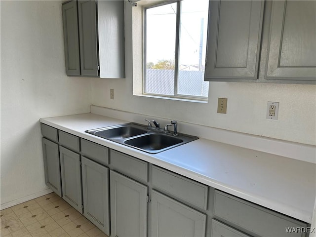 kitchen featuring light floors, light countertops, a sink, and gray cabinetry