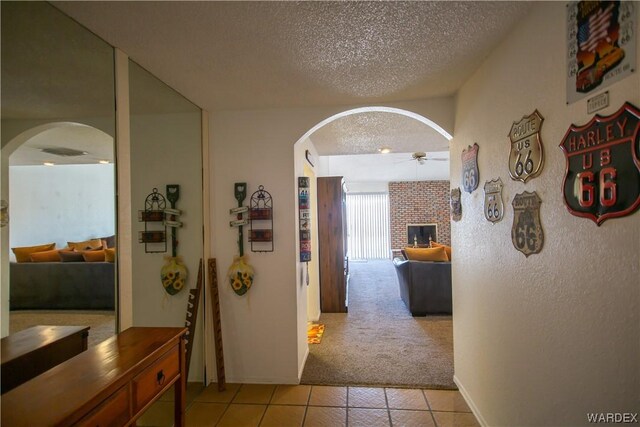 corridor featuring light tile patterned floors, arched walkways, light colored carpet, and a textured ceiling