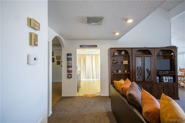 tiled living room with visible vents, arched walkways, carpet floors, and a textured ceiling