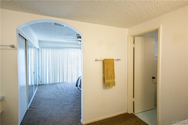 corridor featuring arched walkways, carpet flooring, and a textured ceiling