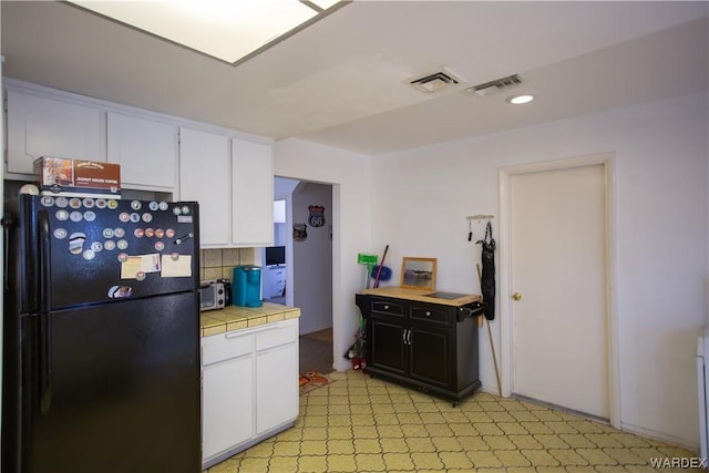 kitchen featuring freestanding refrigerator, tile counters, white cabinetry, and visible vents