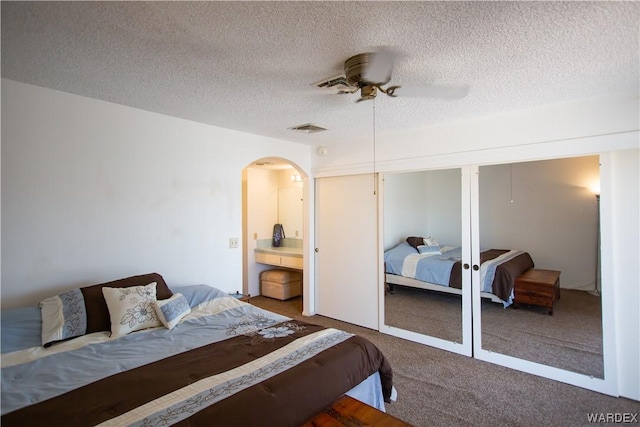 bedroom featuring a closet, a textured ceiling, carpet floors, visible vents, and arched walkways