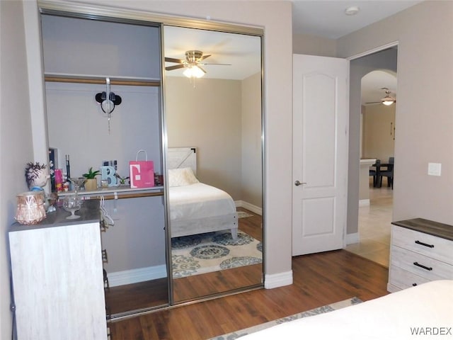 bedroom with arched walkways, a closet, baseboards, and wood finished floors