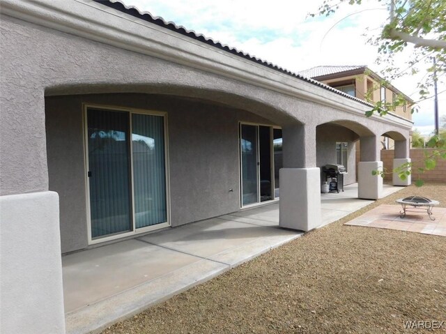 back of house with a tile roof, stucco siding, a fire pit, and a patio