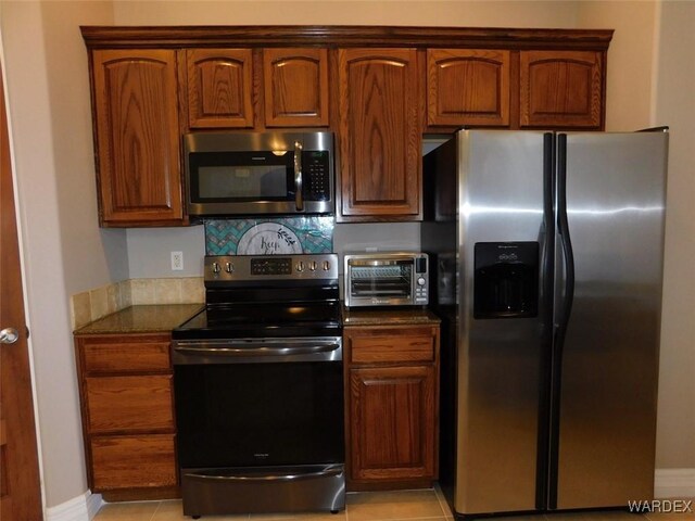 kitchen featuring baseboards, a toaster, dark stone countertops, light tile patterned flooring, and stainless steel appliances