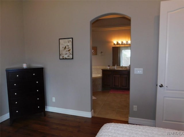 bedroom featuring connected bathroom, baseboards, wood finished floors, arched walkways, and a sink