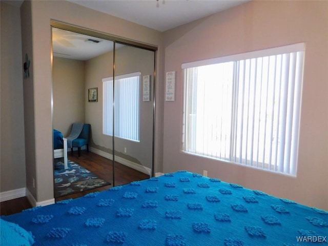 bedroom with wood finished floors, visible vents, a closet, and baseboards