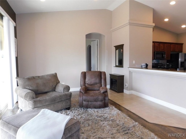 living room with baseboards, lofted ceiling, light wood-style flooring, recessed lighting, and arched walkways