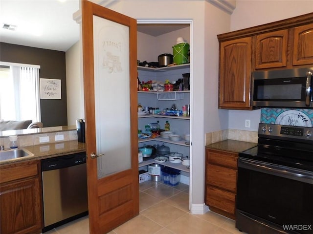 kitchen with light tile patterned floors, stainless steel appliances, visible vents, and brown cabinetry