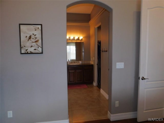 hallway with tile patterned floors, baseboards, arched walkways, and a sink