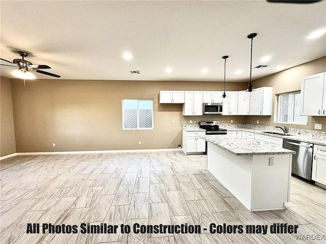 kitchen with appliances with stainless steel finishes, a center island, light stone countertops, white cabinetry, and a sink