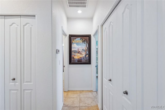 hallway with visible vents, baseboards, and light tile patterned flooring