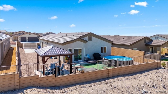 rear view of property featuring stucco siding, a gazebo, a patio area, a fenced backyard, and a tiled roof