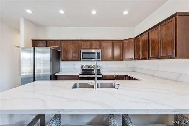 kitchen featuring stainless steel appliances, a breakfast bar, light stone counters, and recessed lighting