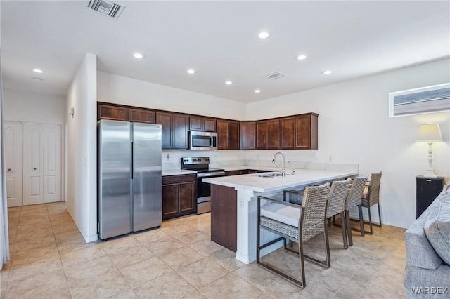 kitchen featuring visible vents, a peninsula, stainless steel appliances, light countertops, and a sink